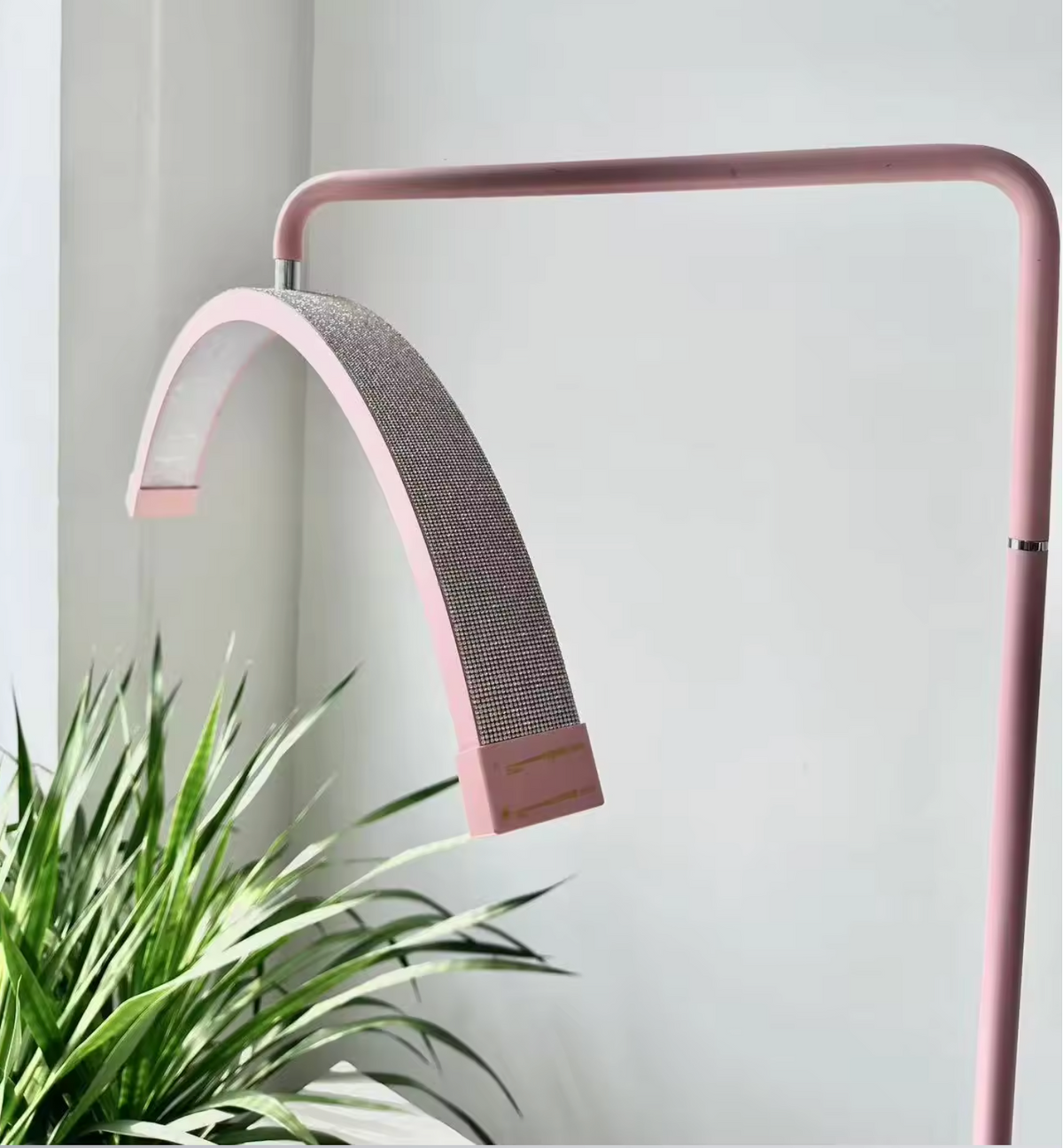 A pink floor lamp with a flexible neck, standing in a relaxed S shape, with a sturdy base. It has a switch on the stem and is connected to a power cord.