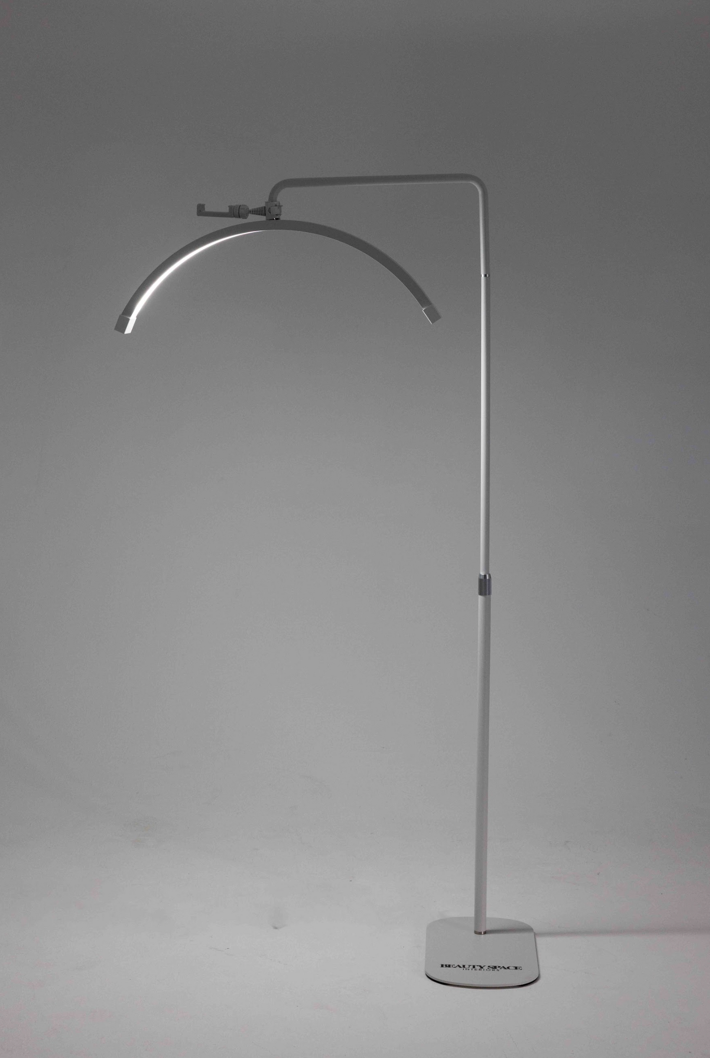 A white floor lamp with a flexible neck, standing in a relaxed S shape, with a sturdy base on the floor. The lamp is illuminated, casting a soft light.