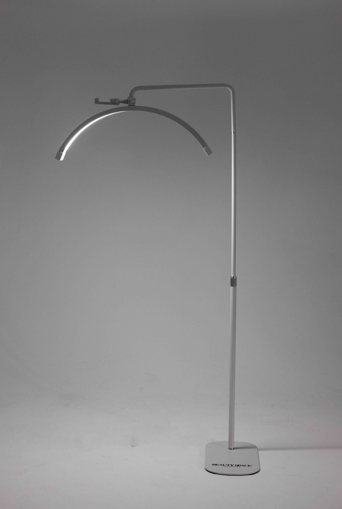 A white floor lamp with a flexible neck, standing in a relaxed S shape, with a sturdy base on the floor. The lamp is illuminated, casting a soft light.