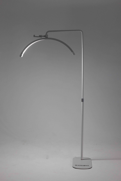 A white floor lamp with a flexible neck, standing in a relaxed S shape, with a sturdy base on the floor. The lamp is illuminated, casting a soft light.